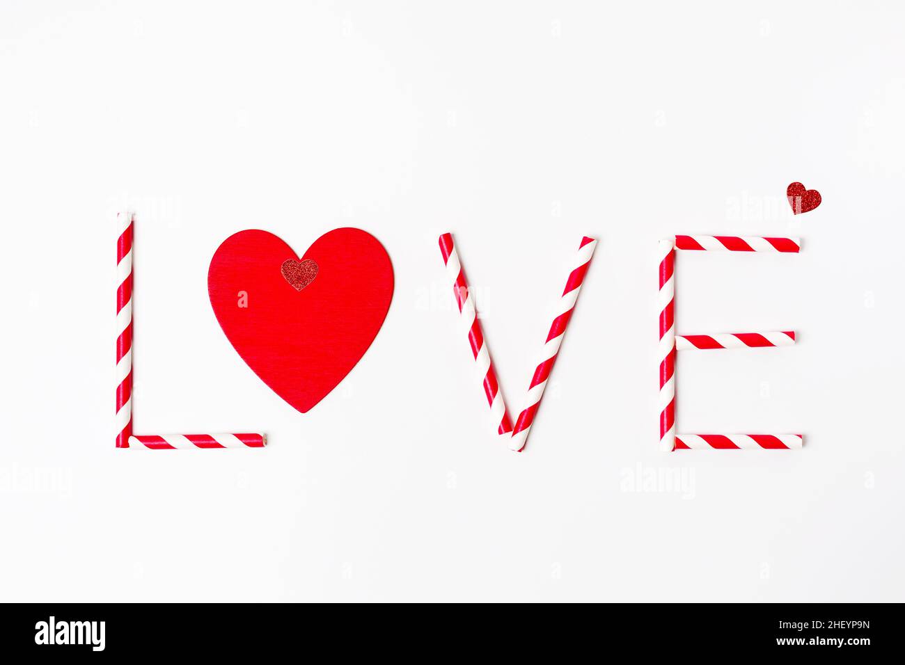 Saint Valentine`s day greeting card, text Love made from striped red and white drinking straws and red heart on white background Stock Photo